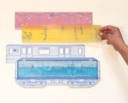 Paper craft detail image of the user playing with the vellum transparent illustrations. Blue vellum is placed on subway car creating a scene of the car being filled with water and a subway rat floating with a pool float. Alternate scenes options are pink disco party and yellow plant filled greenhouse.